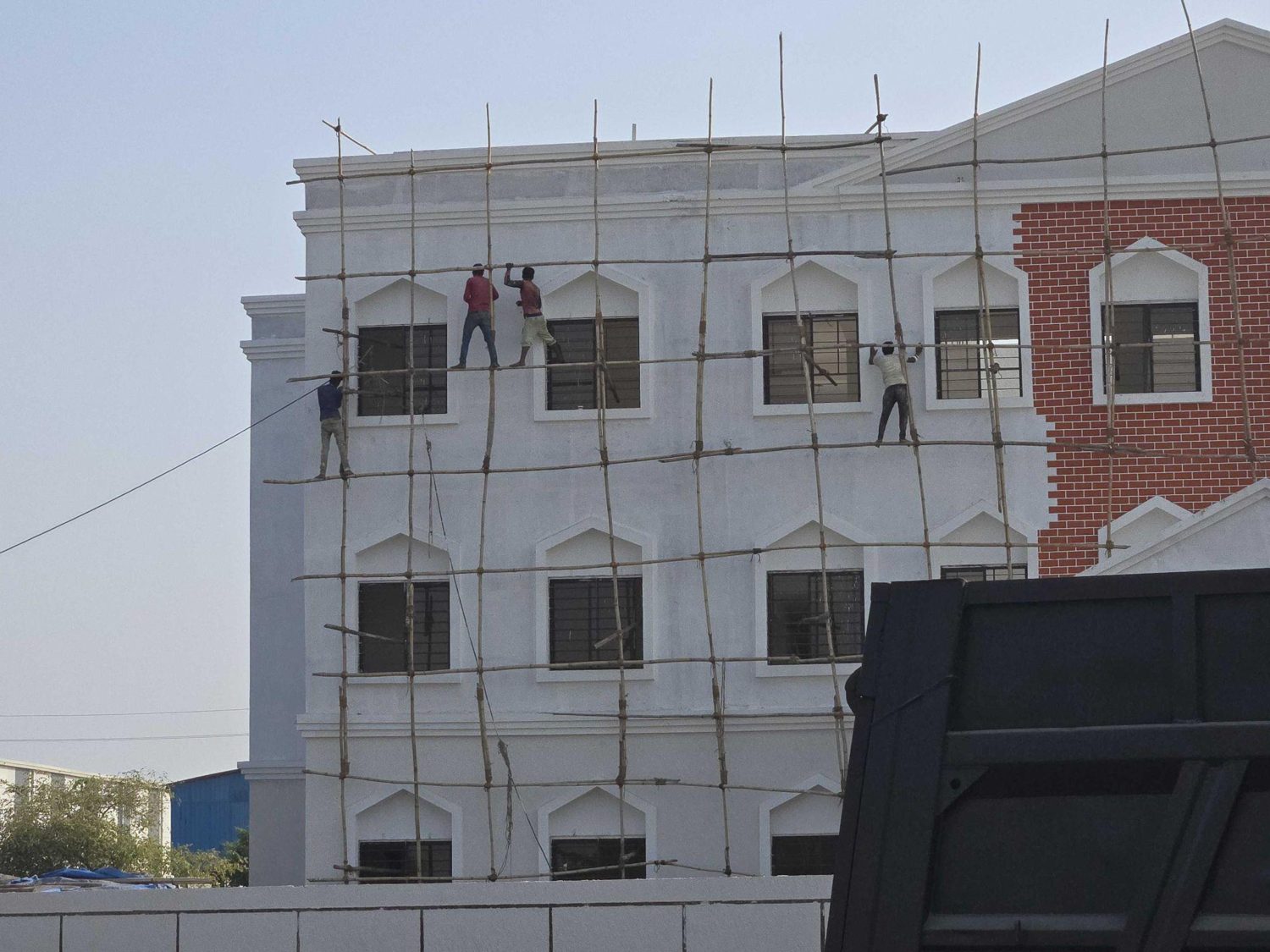 Workers on bamboo scaffolding wrapping a building facade